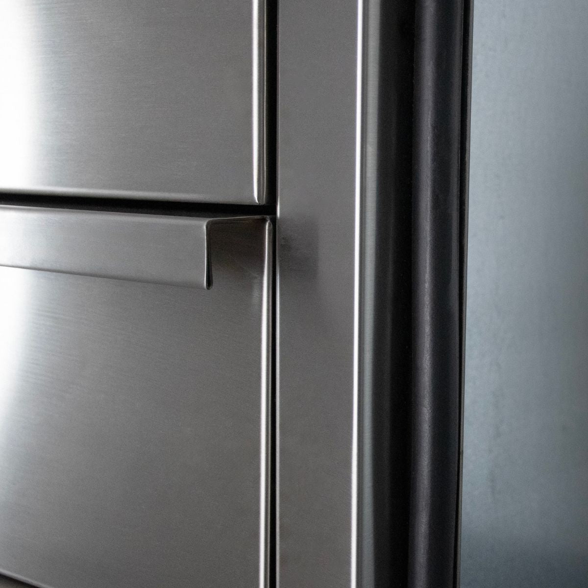 Close-up of a brushed stainless steel refrigerator door with a horizontal handle and dark trim along the edge.