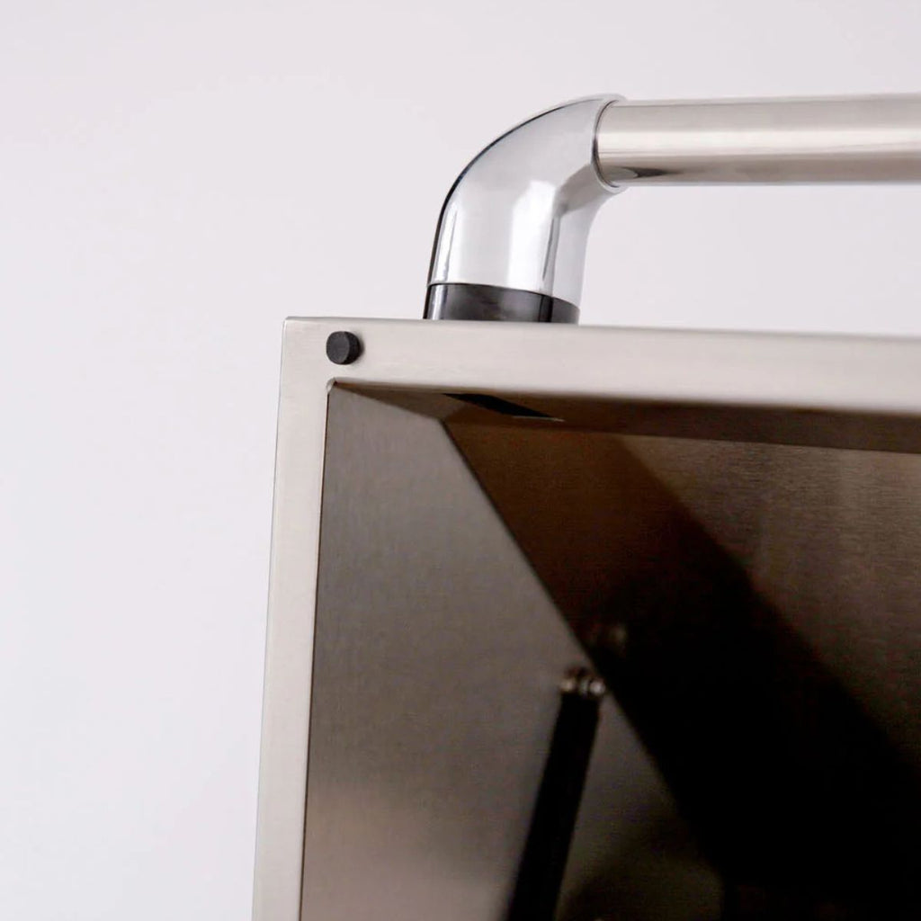 Close-up detail of a stainless steel outdoor grill showing the corner joint, a curved upper handle, and the brushed metal interior.