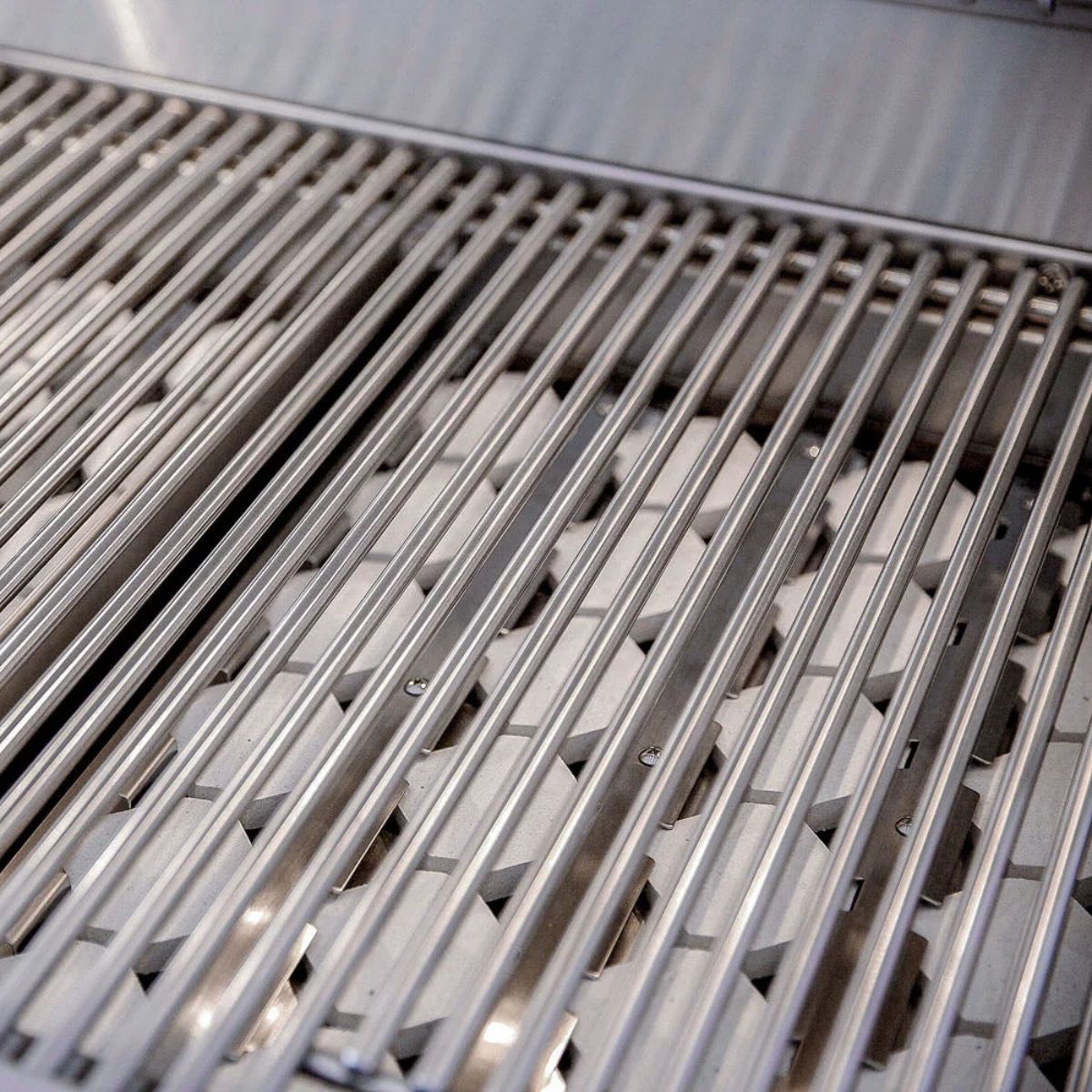 Close-up of stainless steel grill grates with parallel metal bars over a cooking grate surface.