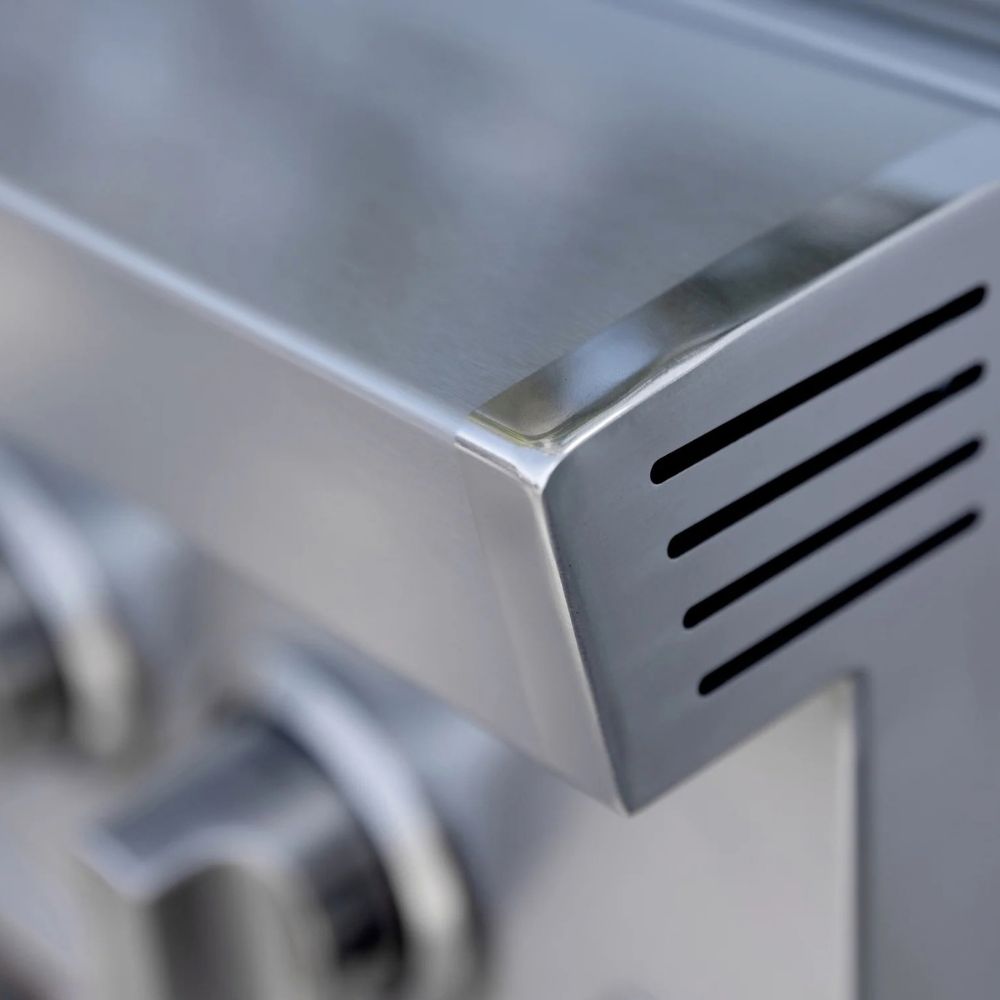 Close-up detail of a stainless steel appliance corner with ventilation slots and blurred control knobs in the background.
