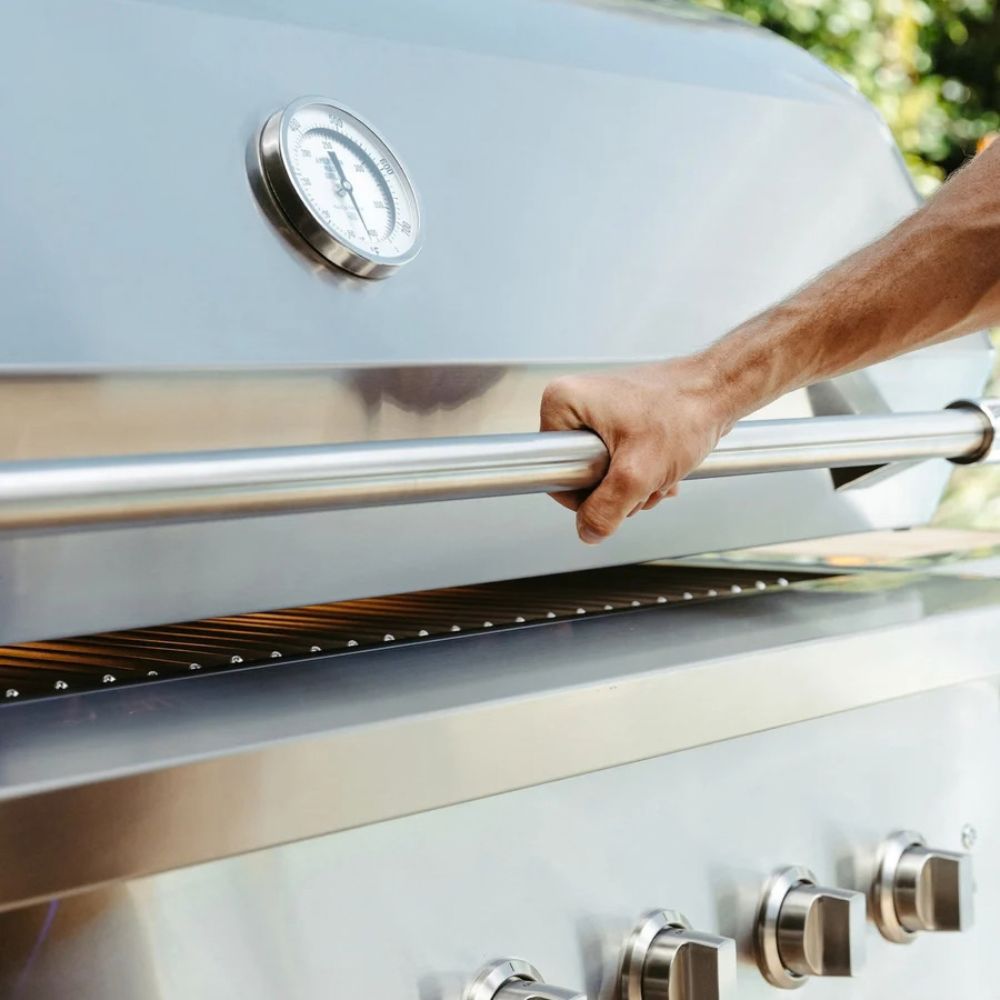 Hand opening a silver barbecue grill with a visible brand logo.