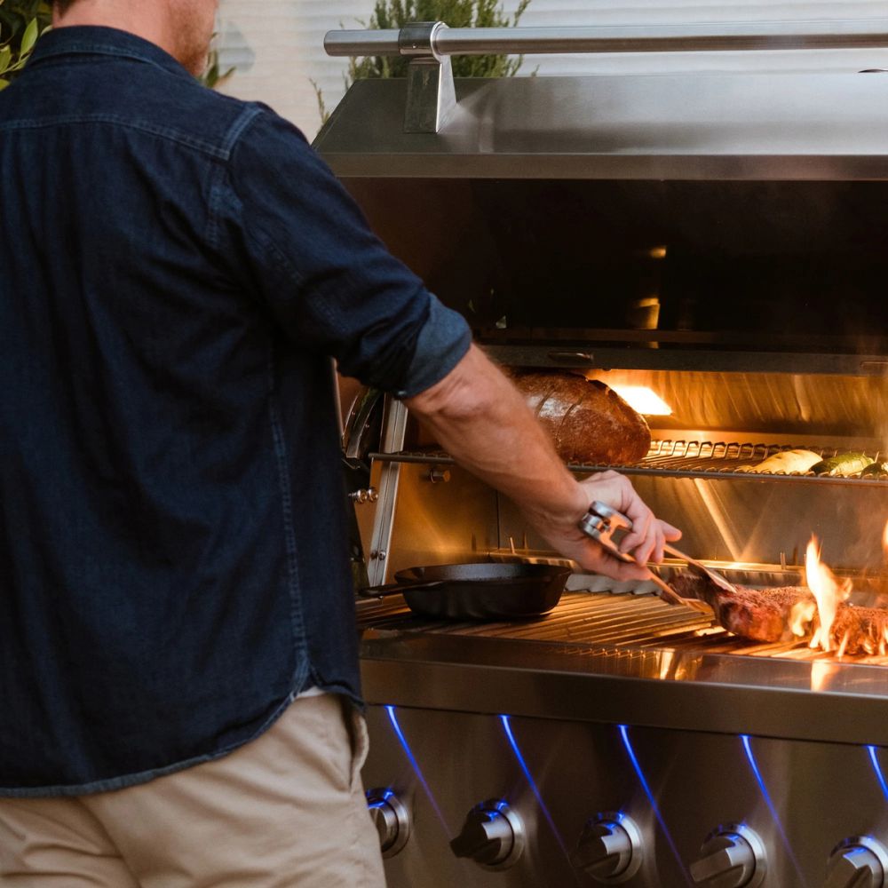 Person grilling on a large outdoor barbecue with flames and smoke.