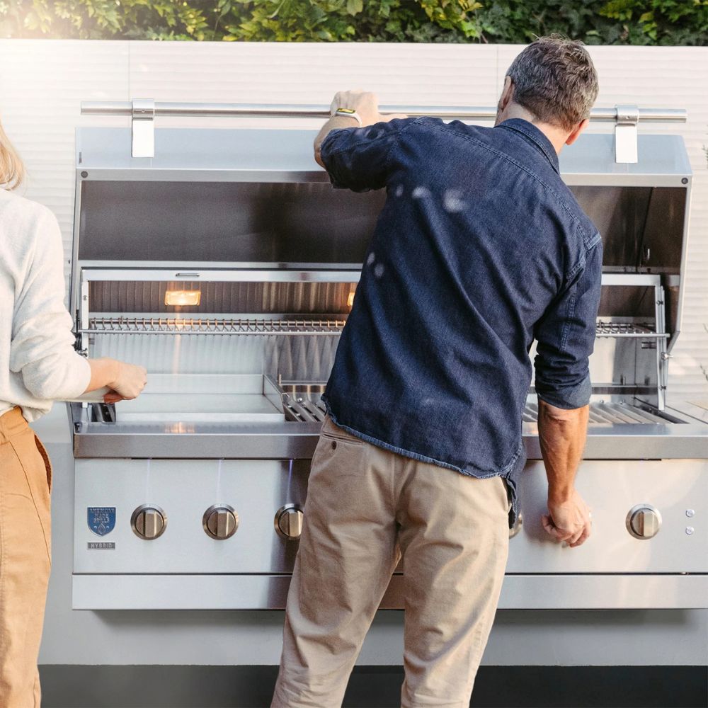 Two people interacting with a large outdoor grill on a patio.