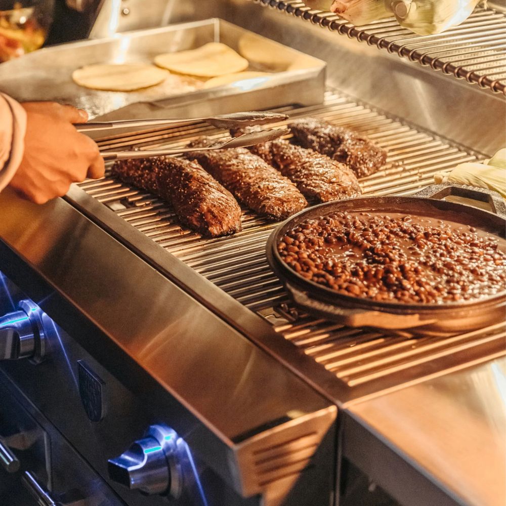 Grilling scene with meats and beans on a stainless steel grill