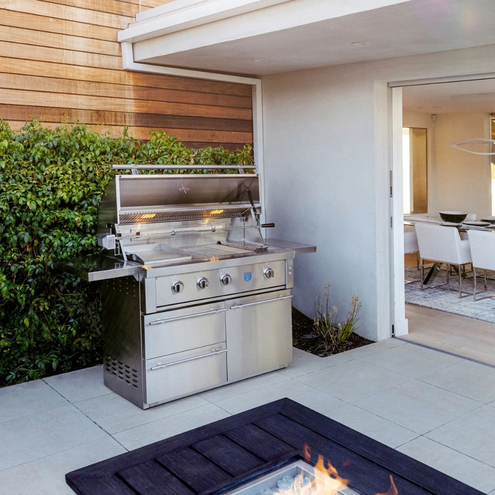 Stainless steel outdoor grill on a patio with a fire pit and garden in the background