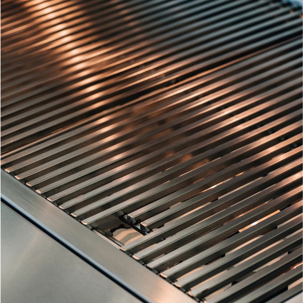 Close-up of stainless steel grill grates with a brushed metal surface and parallel slats, showing warm reflections.