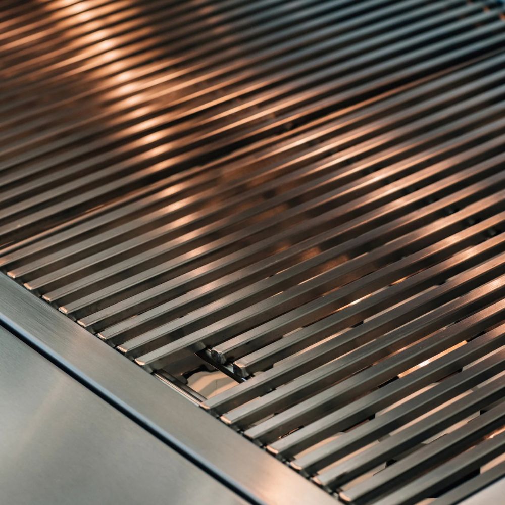 Close-up of stainless steel grill grates with a brushed metal surface and parallel slats under warm lighting.