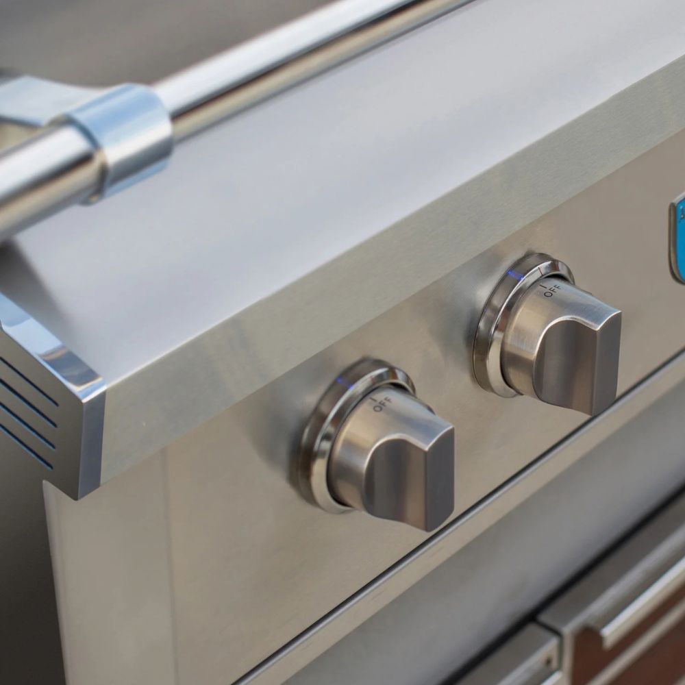 Close-up of stainless steel outdoor grill controls with two silver knobs and a metal handle on a brushed steel surface.