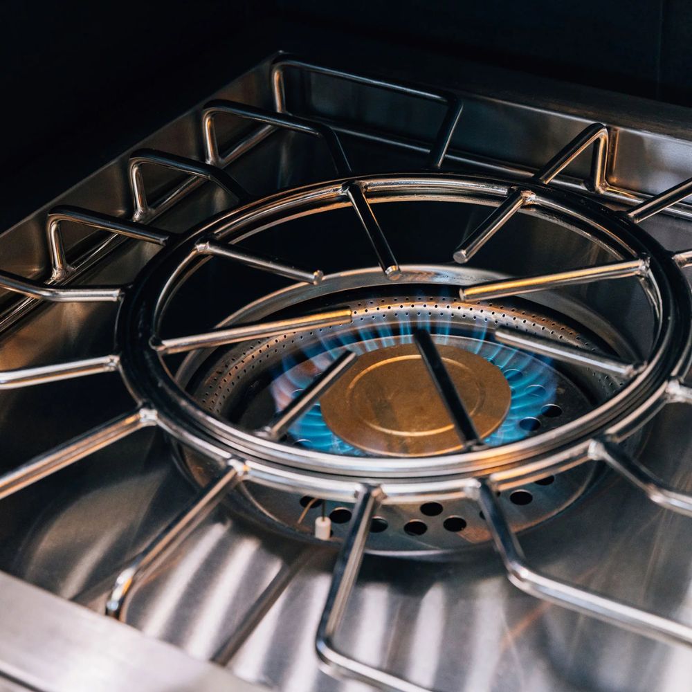 Close-up of a stainless steel gas stove burner with a blue flame ignited beneath a metal grate.