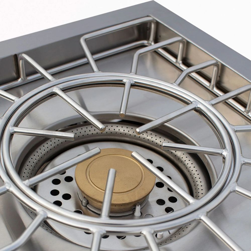 Close-up of a stainless steel gas stove burner with a circular metal grate and a brass burner cap inside a stainless steel pot or burner assembly.