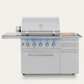 A stainless steel outdoor kitchen island grill with a lid, five front burners with blue flame indicators, a side deck shelf, three drawers, and a wood-grain control panel on a light gray background.