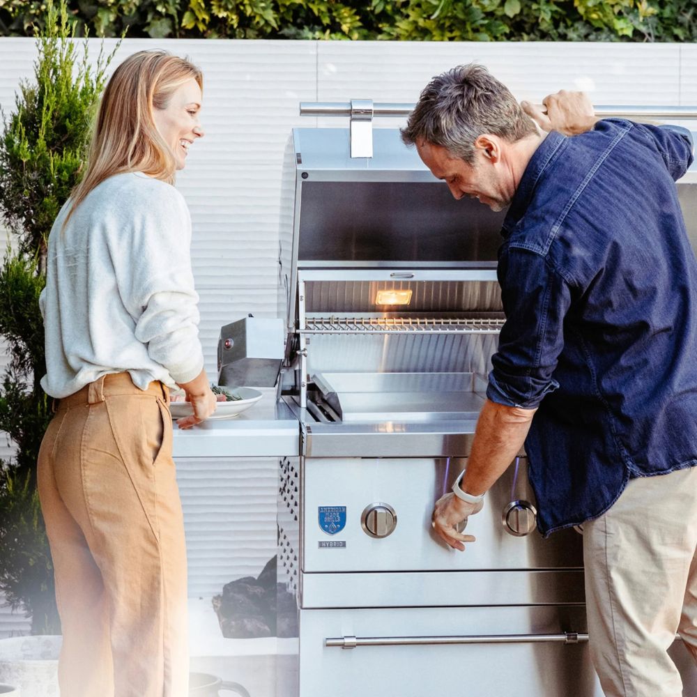 Man and woman interacting with a stainless steel outdoor grill.