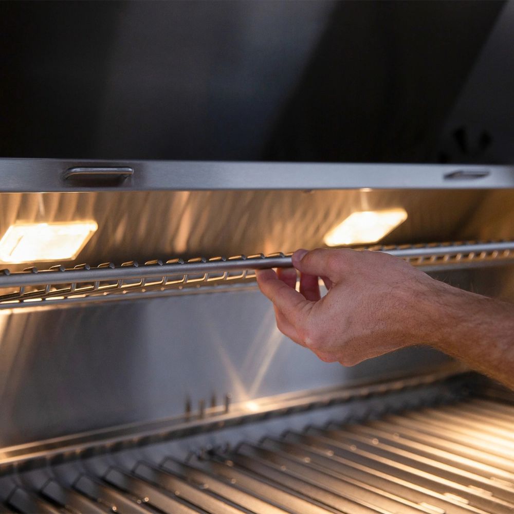 Hand adjusting a metal grill rack inside a barbecue grill.