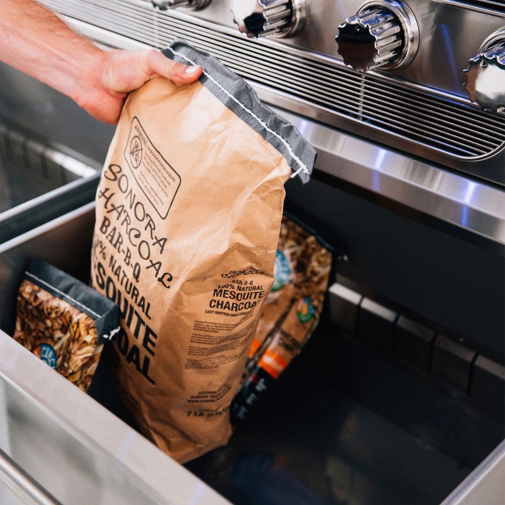 Person holding a bag of Sonora Charcoal in front of a stove.