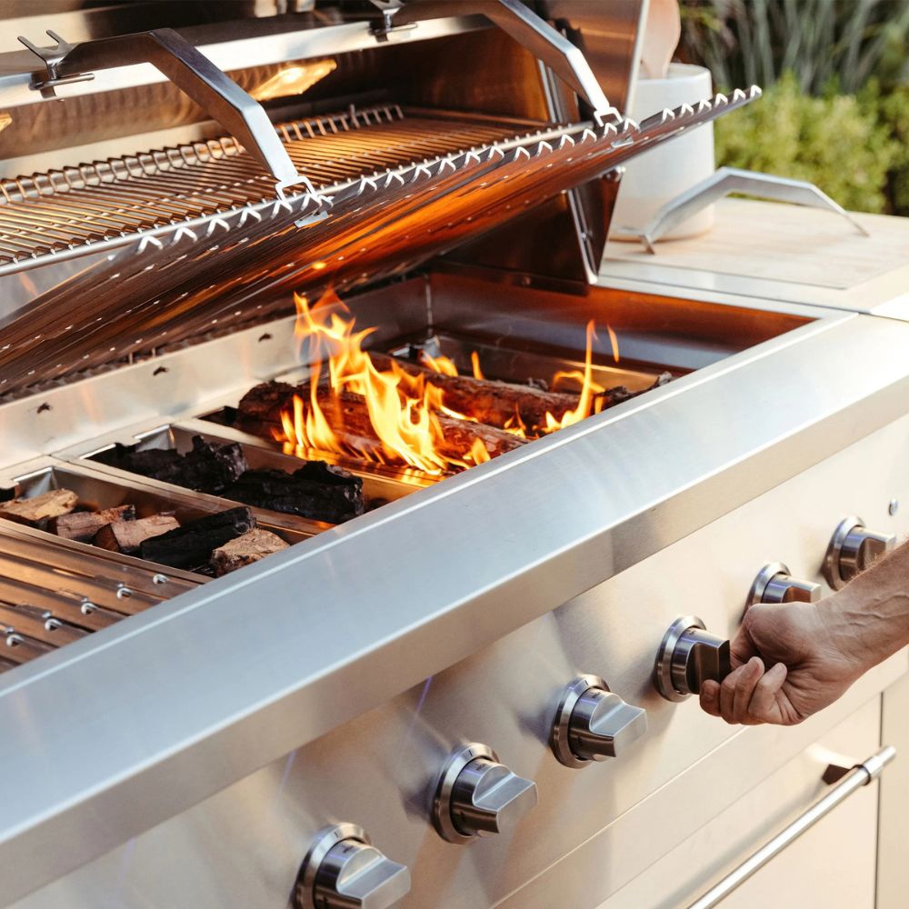 Stainless steel outdoor grill with flames and a hand adjusting a knob.
