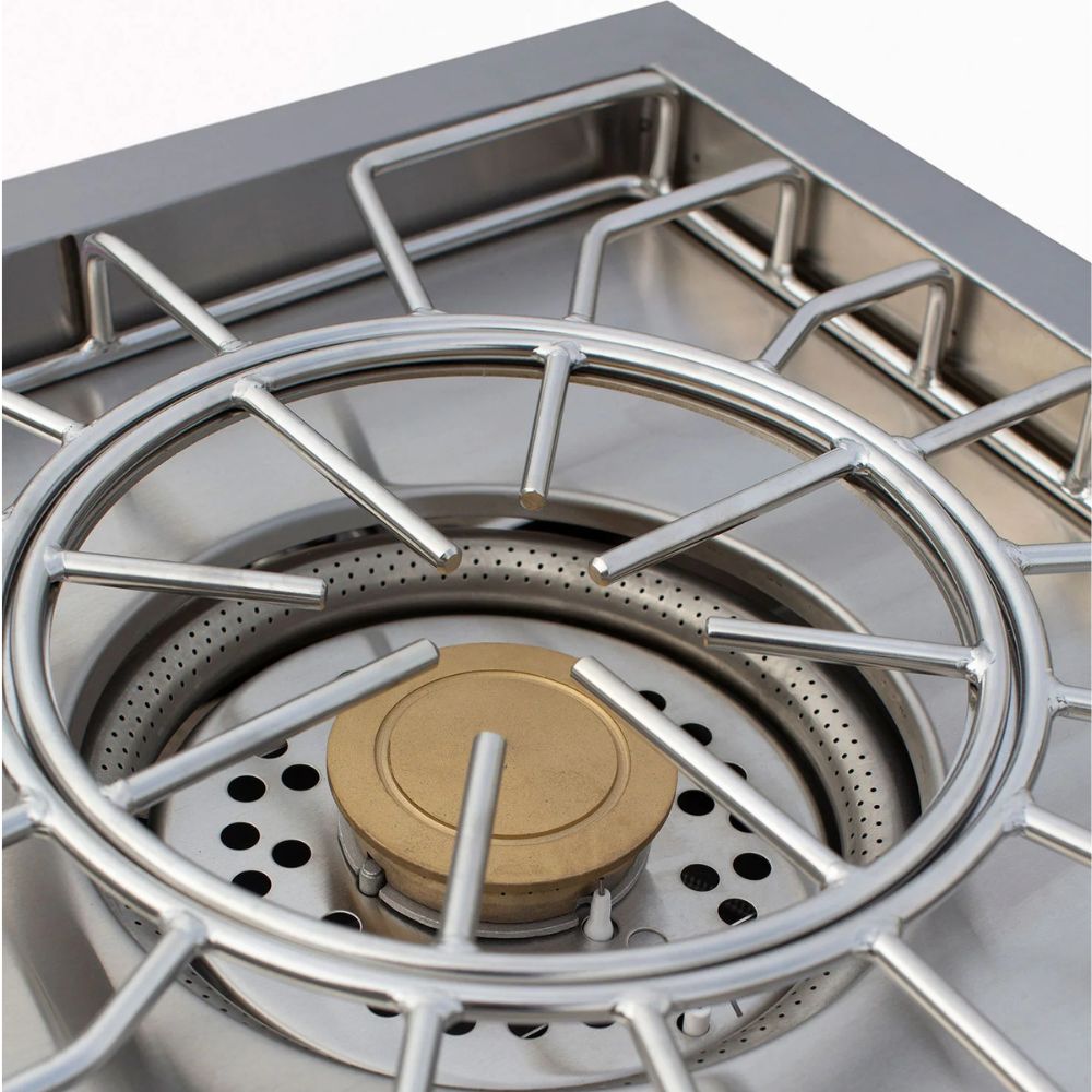 Close-up of a stainless steel gas stove burner with a circular metal grate and a brass burner cap inside a stainless steel pot or burner assembly.