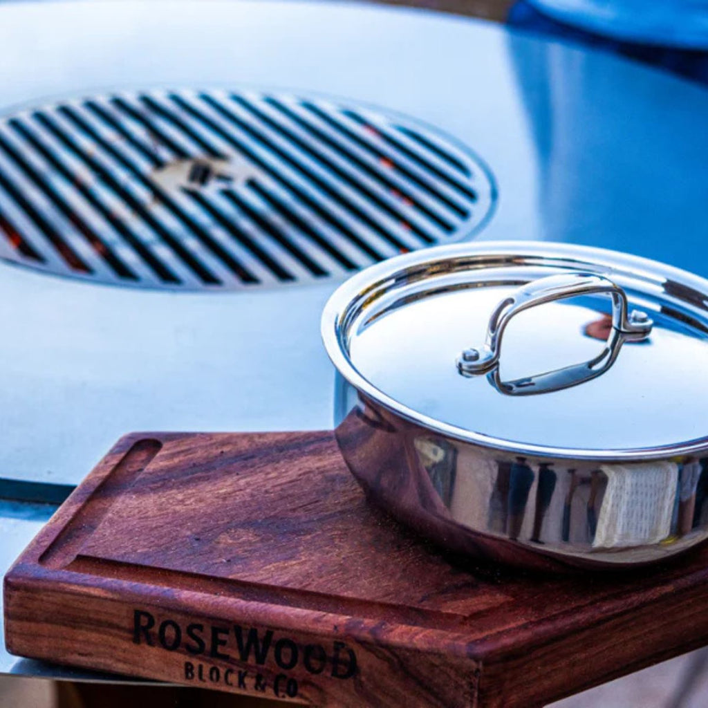 Stainless steel pot with lid on a wooden block labeled 'Rosewood Block & Co' on a blurred background