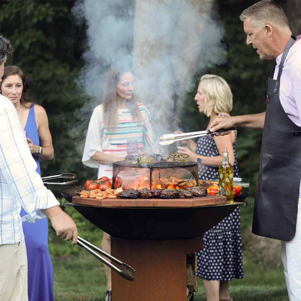 People gathered around a barbecue grill with food being cooked outdoors.