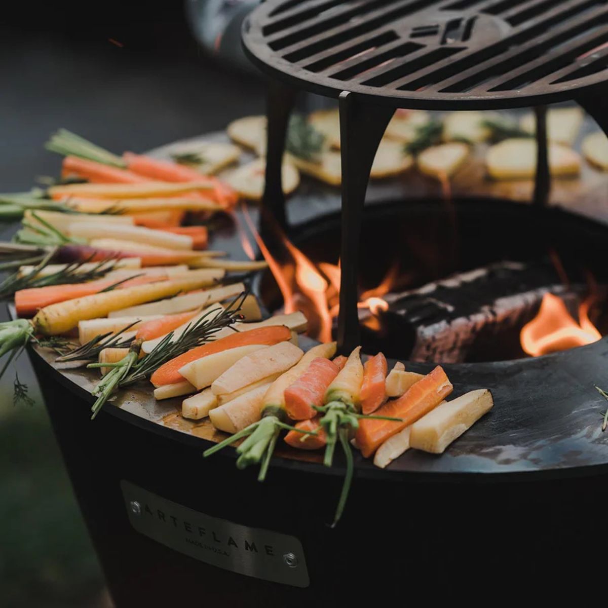 Vegetables being grilled on a portable grill with flames visible