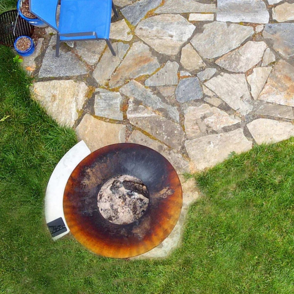 Rust-covered fire pit on a stone patio with grass surrounding it