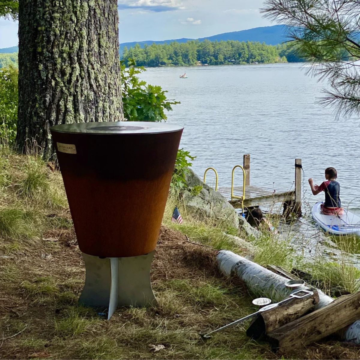 Wood-fired stove by a lake with a person in a kayak in the background