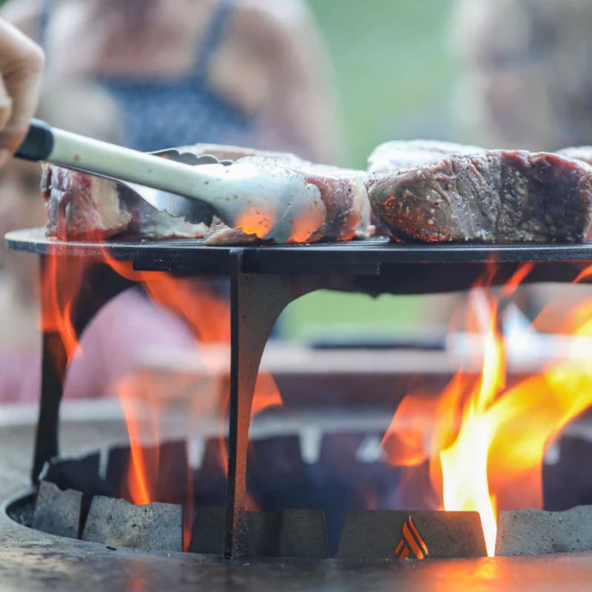Steaks being cooked on a portable grill over an open flame with a blurred background